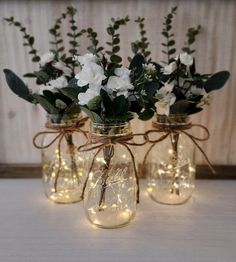 three mason jars filled with flowers and lights