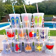 plastic cups with different colored straws and names on them sitting in front of a swimming pool