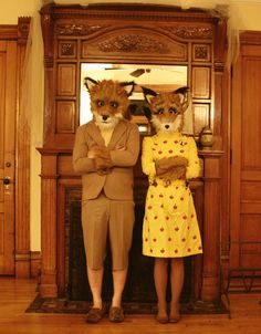 two people dressed as foxes standing in front of a fireplace