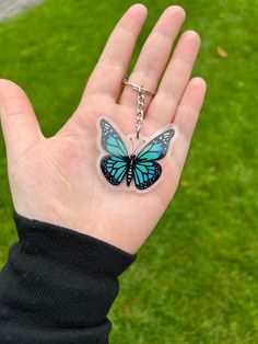 a hand holding a butterfly shaped keychain on it's palm in the grass