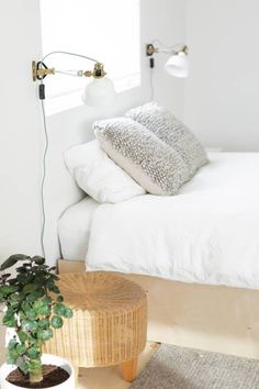 a bed with white sheets and pillows next to a potted plant on the floor