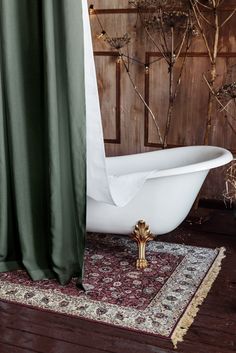 a white bath tub sitting on top of a rug next to a wooden wall with green curtains