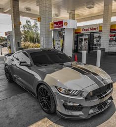 a silver and black mustang parked in front of a gas station with no one around it