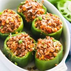 green peppers stuffed with meat and rice in a white casserole dish on a blue cloth