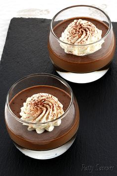 two desserts with whipped cream and chocolate on a black place mat, ready to be eaten