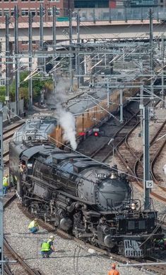 an old fashioned steam engine is on the tracks as workers stand near it and talk