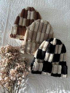 two knitted hats sitting on top of a bed next to dried flowers and leaves