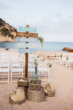 a wooden sign sitting on top of a sandy beach next to chairs and baskets filled with flowers