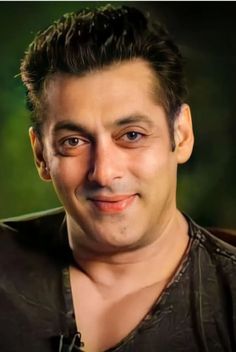 a close up of a person wearing a black shirt and smiling at the camera with green trees in the background