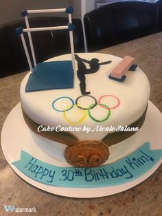 a birthday cake with the olympic symbol on it and some sports related items sitting on top of it