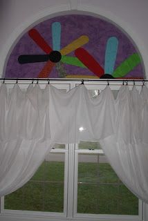 a window with white curtains and an art piece on the top of it's valance