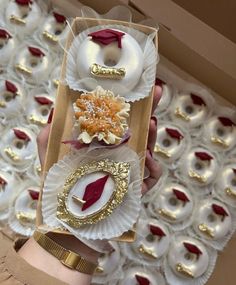 a person is holding two decorative items in a box with gold and red decorations on them