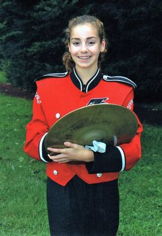 a girl in a red uniform is holding a frisbee and smiling at the camera