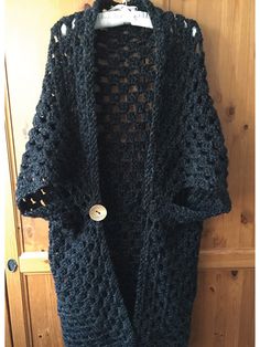 a blue crocheted jacket hanging on a wooden door with a button in it