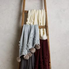 three scarves hanging on a ladder with pom - poms