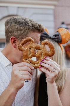 a man and woman kissing while holding pretzels in front of their faces with mickey ears on them