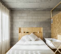 a bed with white sheets and pillows next to a wall made out of plywood