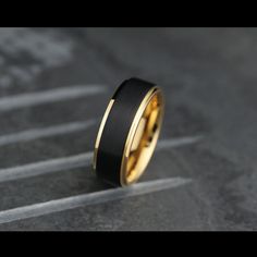 a black and yellow gold wedding ring on top of a gray surface with the word love written in it