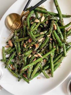 a white plate topped with green beans and almonds next to a gold serving spoon