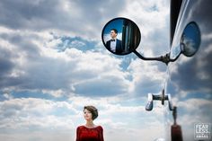 a woman standing in front of a truck with a man's face reflected in the mirror