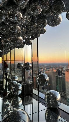 a room with many shiny balls hanging from it's ceiling and windows overlooking the city