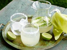 a pitcher and two glasses sitting on a plate with limes next to each other