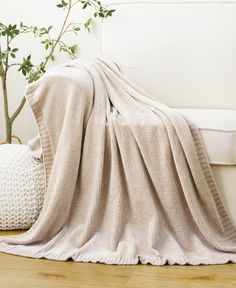 a white couch with a blanket on top of it next to a potted plant