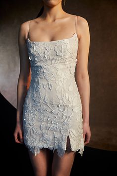 a woman in a short white dress posing for a photo with her hair pulled back