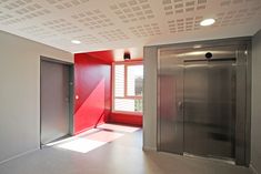 an empty room with red walls and two elevators in the center, next to a large open door