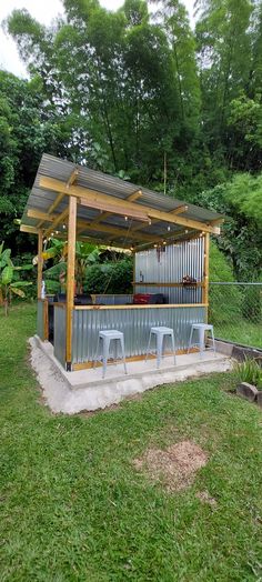 an outdoor bar in the middle of a grassy area with stools and lights on it