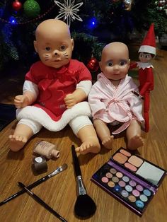 two baby dolls sitting next to each other on a table with makeup and cosmetics in front of them