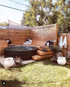 an outdoor hot tub in the middle of a yard with wooden fence and potted plants