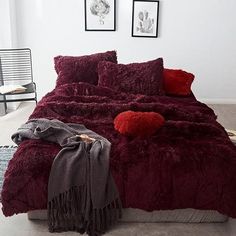 a bed with red comforter and pillows in a room next to pictures on the wall