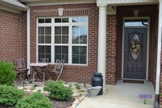 the front door of a brick house with chairs and table in it's yard