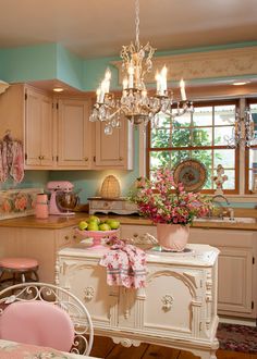 a pink and white kitchen with chandelier above the island in front of it