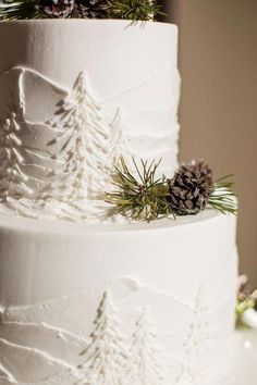 a white wedding cake decorated with pine cones and evergreen trees