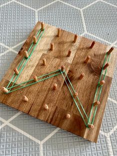 a wooden board with green string and pegs on the top, sitting on a white tile floor