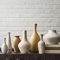 five vases lined up on top of a wooden table in front of a brick wall