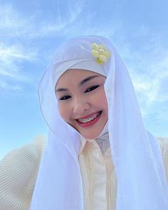 a woman wearing a white veil with a flower on it's head and smiling at the camera