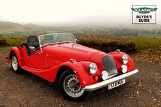 an old red sports car parked on the side of a road with hills in the background