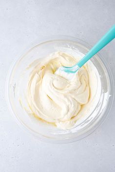 a bowl filled with whipped cream on top of a white counter next to a blue spoon