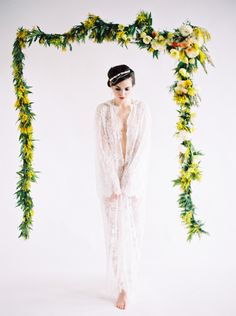 a woman is standing in front of a floral arch