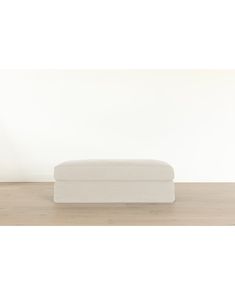 a white ottoman sitting on top of a hard wood floor next to a white wall