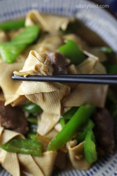 a blue and white bowl filled with pasta and veggies next to chopsticks