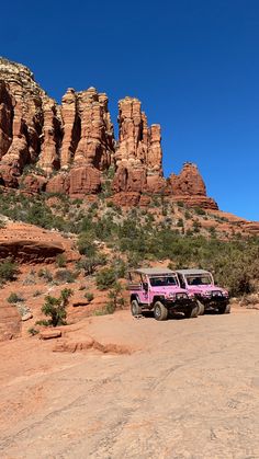 two pink jeeps parked in front of some red rocks