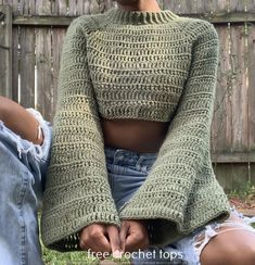 a woman sitting on the ground wearing a green knitted sweater and ripped denim shorts