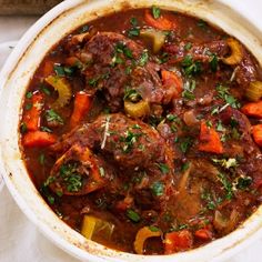 a pot filled with meat and vegetables on top of a white table next to a bowl of salad