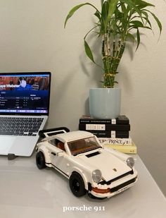 a laptop computer sitting on top of a desk next to a toy car and potted plant