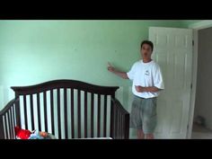 a man standing in front of a crib pointing at the wall with his finger