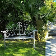 a white bench sitting in the middle of a lush green park next to palm trees